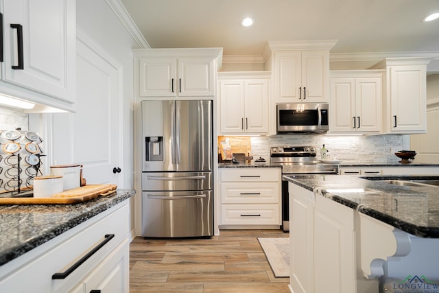 kitchen with light wood-type flooring, dark stone countertops, white cabinetry, appliances with stainless steel finishes, and crown molding