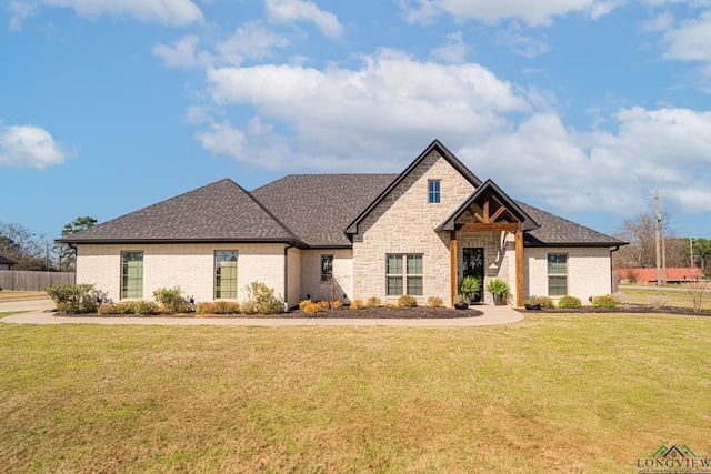 view of front facade with brick siding, a front lawn, and roof with shingles