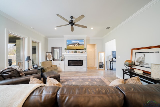 living area featuring visible vents, light wood finished floors, ceiling fan, a glass covered fireplace, and crown molding