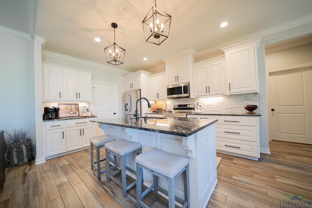 kitchen featuring light wood-type flooring, ornamental molding, a kitchen breakfast bar, appliances with stainless steel finishes, and white cabinets