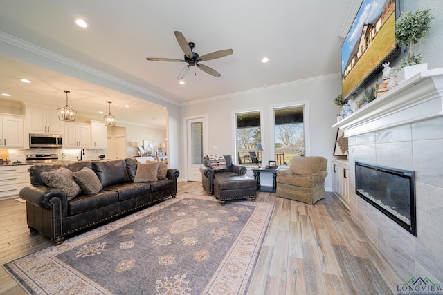 living area featuring light wood-type flooring, ornamental molding, ceiling fan with notable chandelier, recessed lighting, and a fireplace