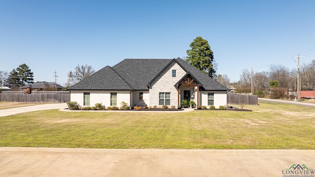 view of front of home featuring stone siding, roof with shingles, a front yard, and fence