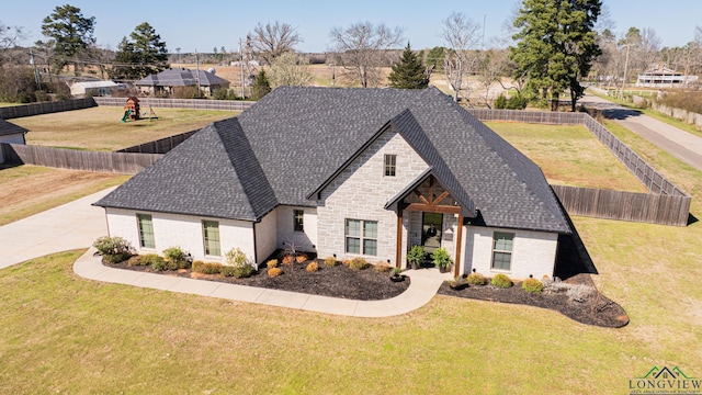 view of front of property with a front yard, a fenced backyard, stone siding, and a shingled roof