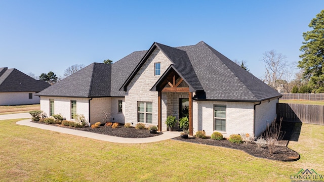 view of front of home with a front yard, fence, a shingled roof, stone siding, and brick siding