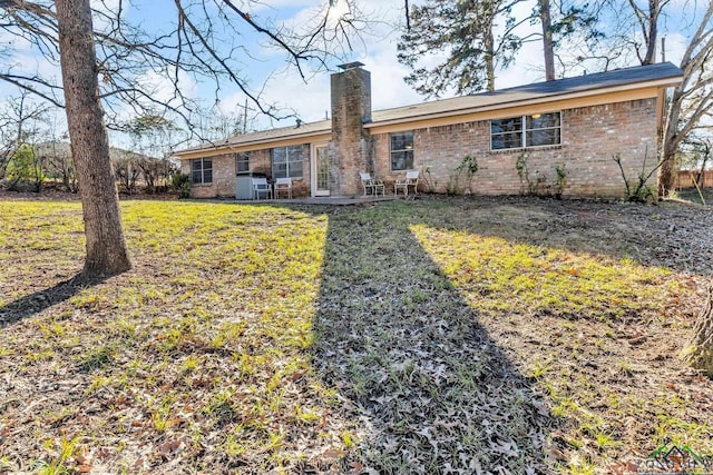 back of house featuring brick siding, a lawn, and a chimney