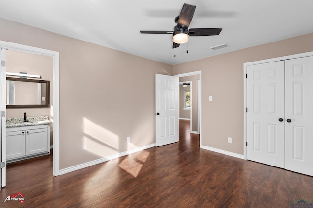 unfurnished bedroom with ensuite bathroom, indoor wet bar, dark hardwood / wood-style flooring, ceiling fan, and a closet