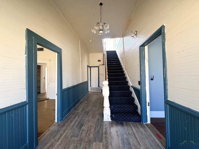 stairway with a wainscoted wall, wood finished floors, and a chandelier