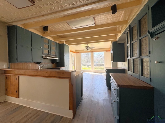 kitchen featuring wood finished floors, a peninsula, an ornate ceiling, butcher block countertops, and under cabinet range hood