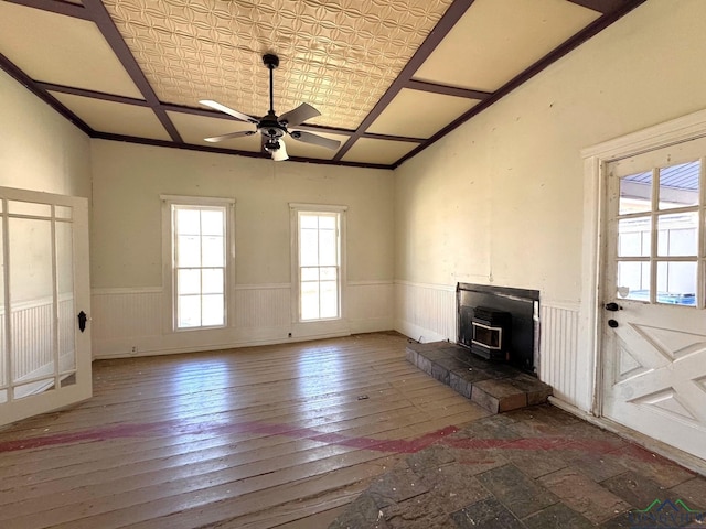 unfurnished living room featuring ceiling fan, a wainscoted wall, a wood stove, hardwood / wood-style flooring, and an ornate ceiling