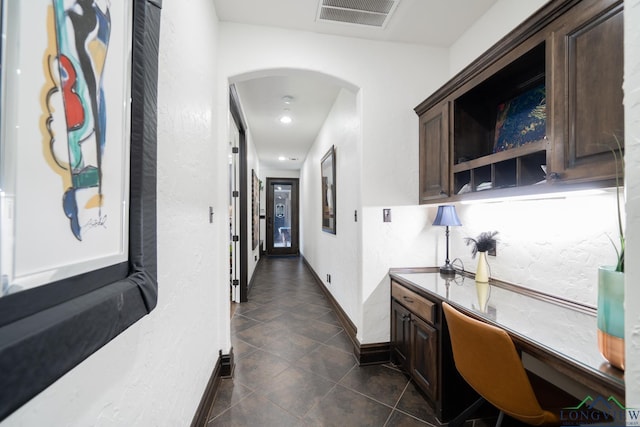 hall featuring arched walkways, dark tile patterned flooring, visible vents, and baseboards