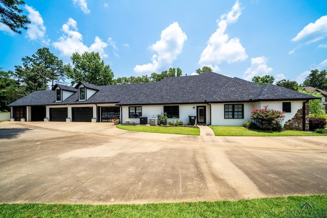 view of front of property featuring roof with shingles, concrete driveway, a front yard, central AC, and a garage