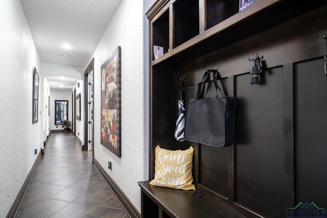 mudroom with arched walkways, dark tile patterned flooring, a textured wall, and baseboards