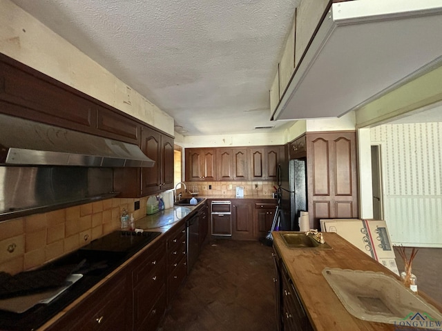 kitchen featuring sink, a textured ceiling, black refrigerator, range hood, and backsplash