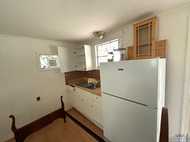 kitchen with white refrigerator, white cabinetry, sink, and backsplash