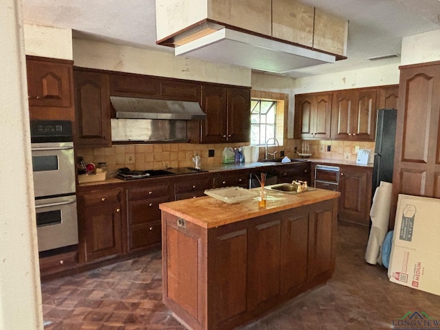 kitchen featuring butcher block countertops, sink, backsplash, black appliances, and a center island with sink