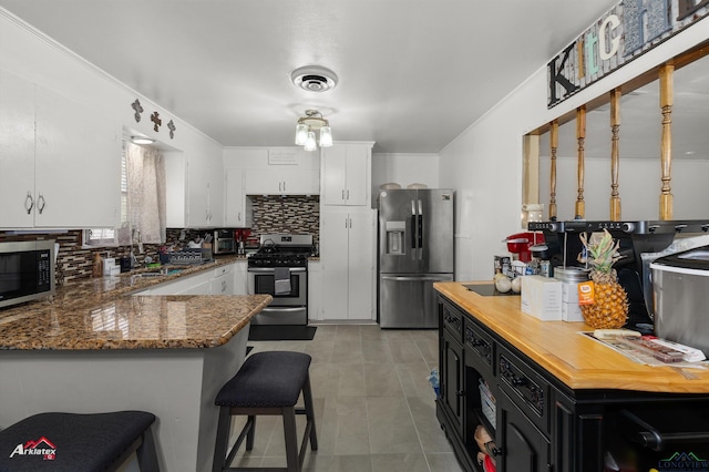 kitchen with stainless steel appliances, tasteful backsplash, white cabinets, and a peninsula