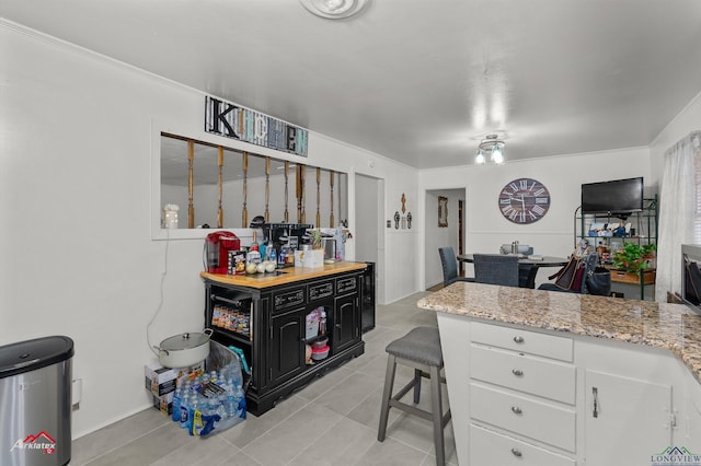 kitchen with light tile patterned flooring, light stone counters, white cabinetry, ornamental molding, and a breakfast bar