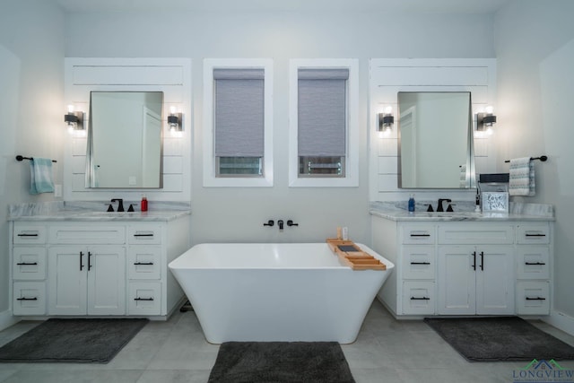 bathroom with tile patterned flooring, a freestanding bath, two vanities, and a sink