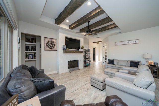 living area featuring a large fireplace, visible vents, a ceiling fan, light wood-style flooring, and beamed ceiling