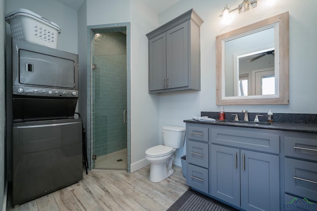 full bathroom with toilet, wood finished floors, vanity, stacked washing maching and dryer, and a shower stall