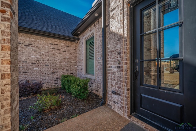 property entrance featuring brick siding and a shingled roof