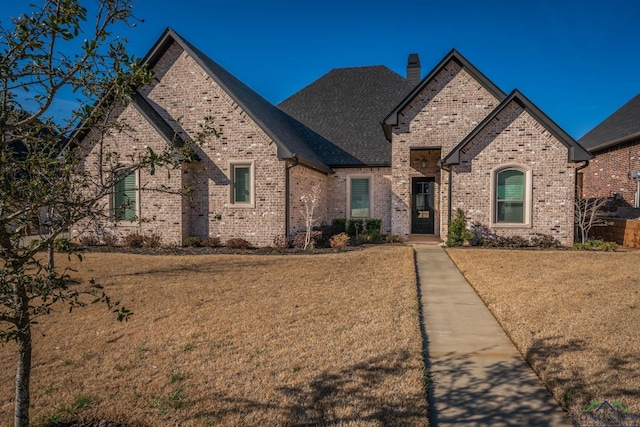 french provincial home with a shingled roof, a chimney, a front lawn, and brick siding