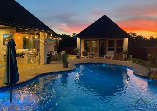 pool at dusk with an outbuilding, an outdoor kitchen, fence, a fenced in pool, and a patio area