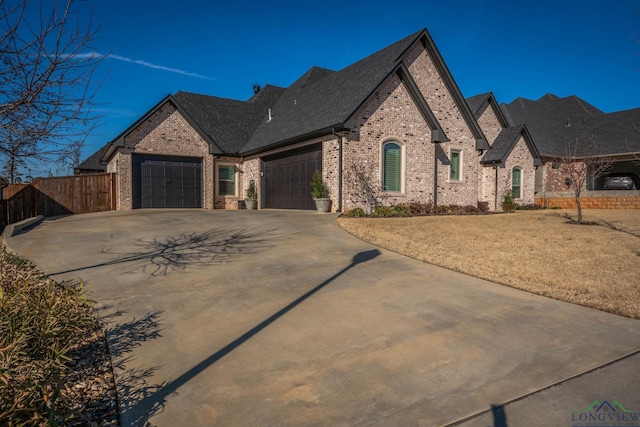 french provincial home with a garage, driveway, fence, and brick siding