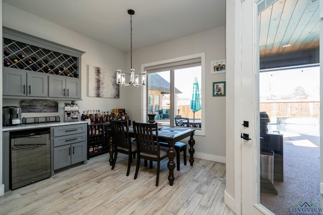 dining space featuring light wood finished floors, a bar, a chandelier, beverage cooler, and baseboards