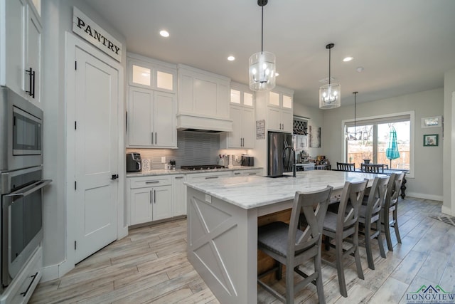 kitchen with a kitchen island with sink, stainless steel oven, white cabinets, freestanding refrigerator, and glass insert cabinets