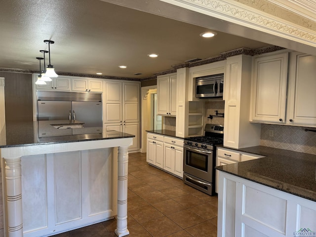 kitchen featuring hanging light fixtures, dark tile patterned floors, decorative backsplash, white cabinets, and appliances with stainless steel finishes