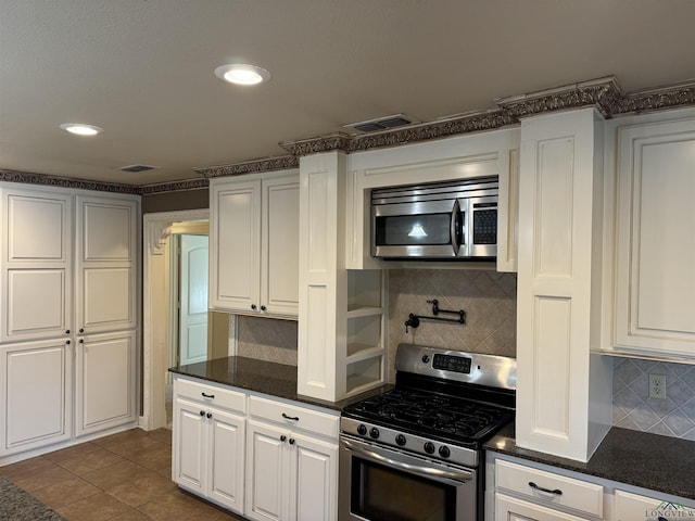 kitchen featuring decorative backsplash, white cabinetry, dark tile patterned floors, and stainless steel appliances