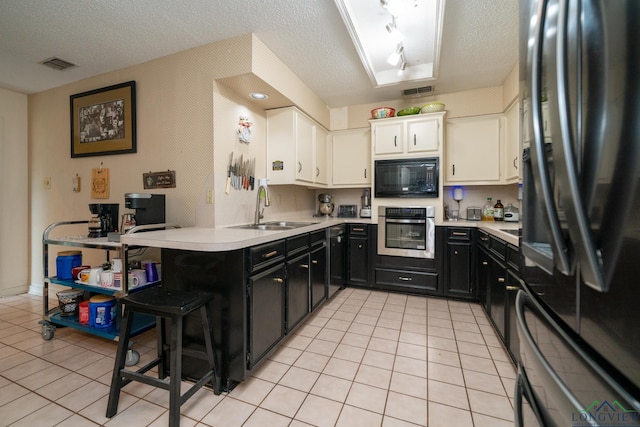 kitchen featuring sink, kitchen peninsula, a textured ceiling, white cabinets, and black appliances