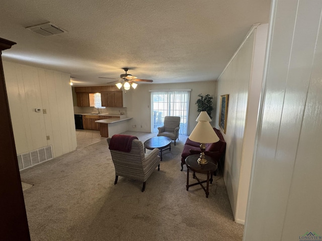 living room with ceiling fan, sink, wood walls, light colored carpet, and a textured ceiling