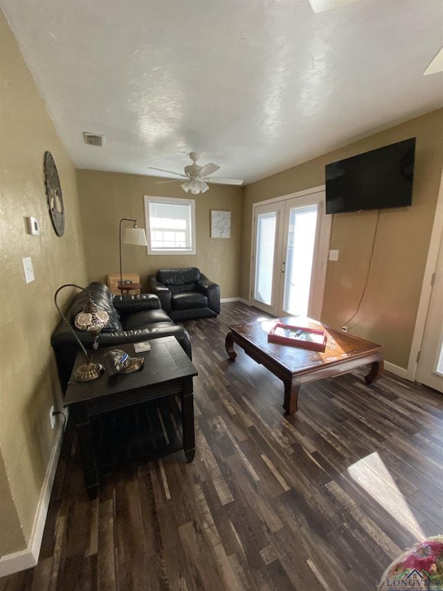 living room featuring dark wood-type flooring, visible vents, baseboards, and a ceiling fan