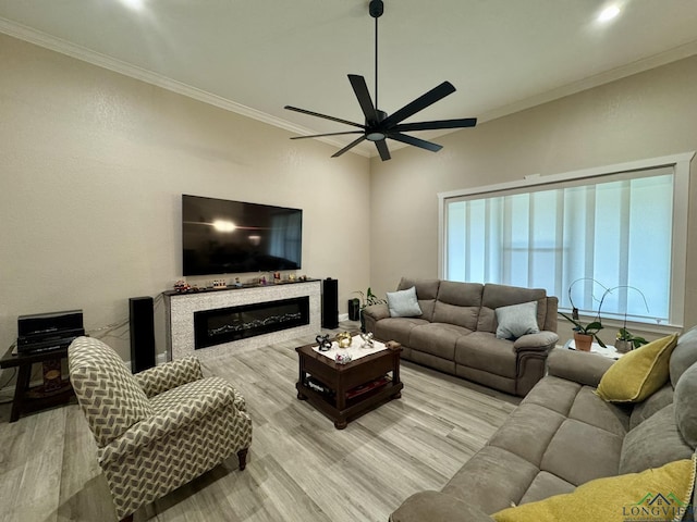 living area with wood finished floors, ceiling fan, ornamental molding, and a glass covered fireplace
