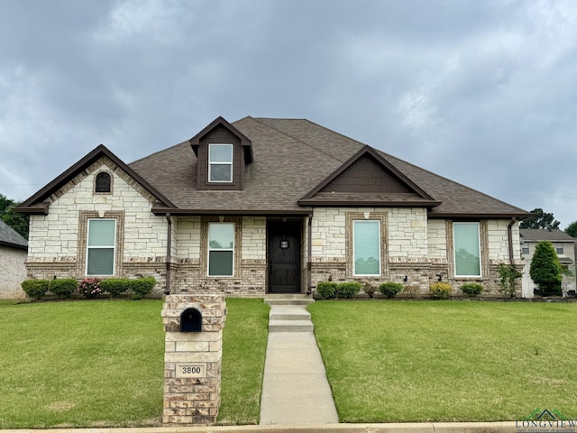 view of front of home featuring a front yard, stone siding, and roof with shingles