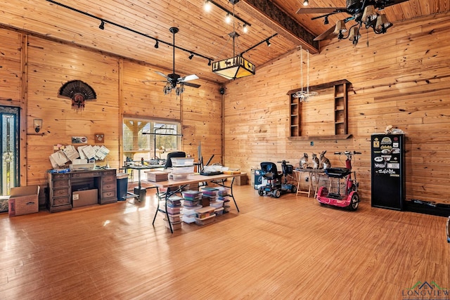 office area featuring a towering ceiling, wood finished floors, a ceiling fan, and wooden walls