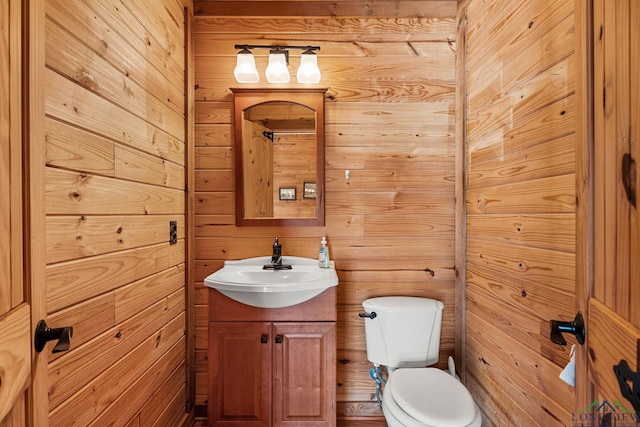 half bathroom featuring vanity, toilet, and wooden walls