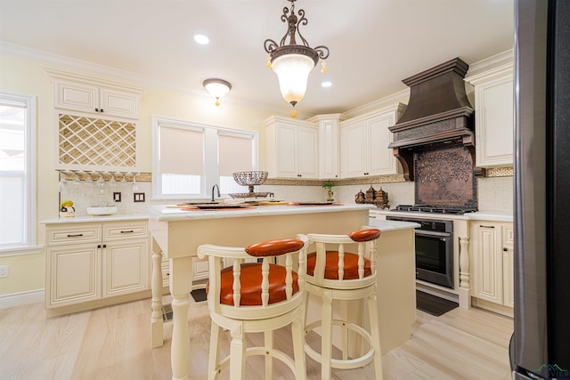 kitchen featuring light wood-type flooring, ornamental molding, custom exhaust hood, stainless steel appliances, and decorative light fixtures