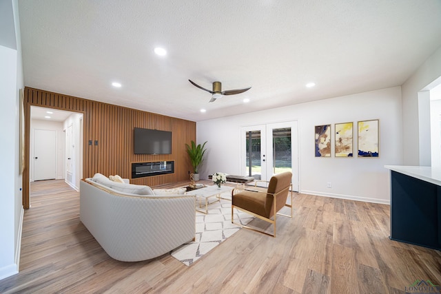 living room with ceiling fan, french doors, light hardwood / wood-style floors, a textured ceiling, and wooden walls