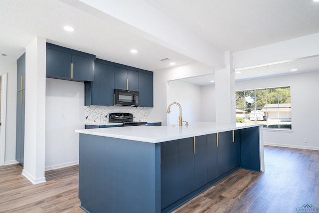 kitchen featuring backsplash, a kitchen island with sink, black appliances, sink, and light hardwood / wood-style flooring