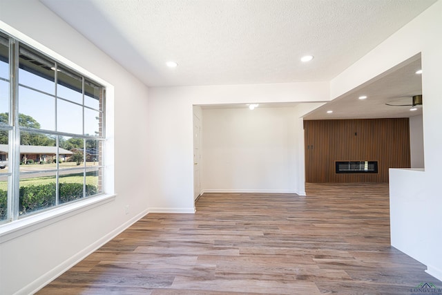 spare room with a fireplace, a textured ceiling, light hardwood / wood-style floors, and ceiling fan