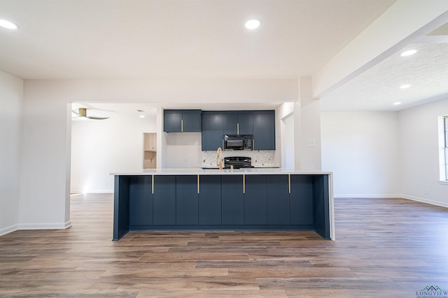 kitchen featuring black appliances, decorative backsplash, light hardwood / wood-style floors, and a breakfast bar area