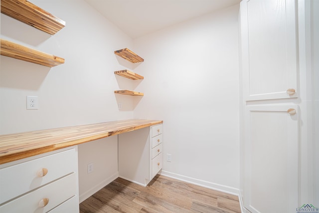 spacious closet with light wood-type flooring and built in desk