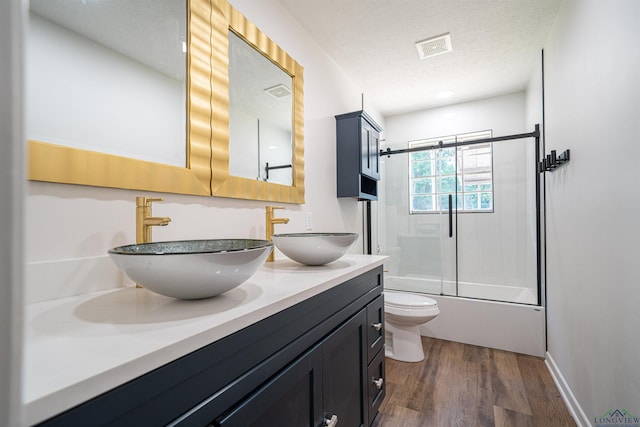 full bathroom featuring bath / shower combo with glass door, vanity, a textured ceiling, hardwood / wood-style flooring, and toilet