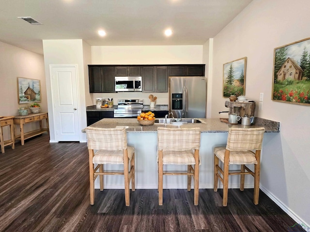 kitchen featuring visible vents, a peninsula, a breakfast bar, appliances with stainless steel finishes, and dark wood-style floors