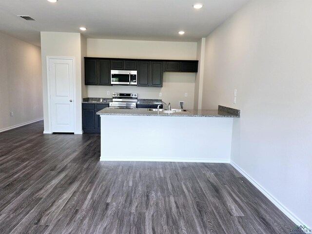 kitchen featuring visible vents, stainless steel appliances, a sink, dark cabinets, and dark wood-style floors