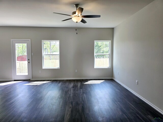 unfurnished room featuring baseboards, dark wood finished floors, ceiling fan, and plenty of natural light