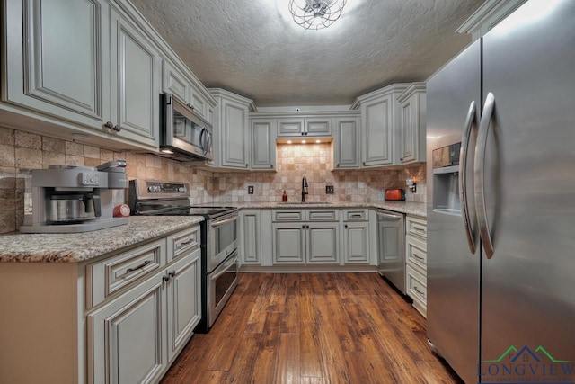 kitchen with sink, appliances with stainless steel finishes, tasteful backsplash, light stone countertops, and dark hardwood / wood-style flooring